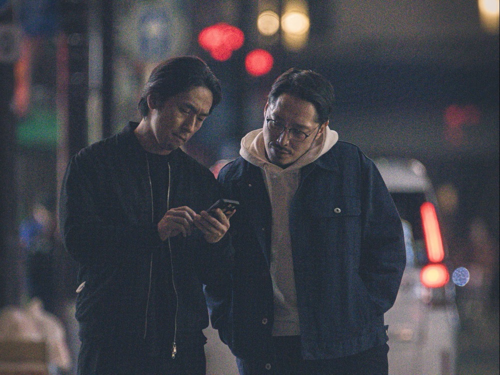 夜の繁華街でスマホを見ながら店を探す2人